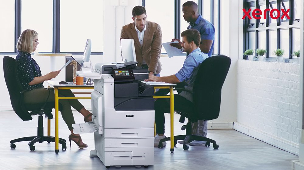 Trabajadores de oficina colaborando cerca de una impresora Xerox. Trabajadores de oficina colaborando cerca de una impresora Xerox.