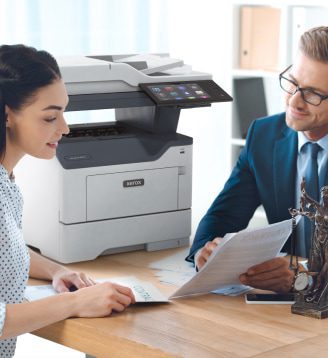 Un hombre y una mujer sentados a una mesa conversan mientras hay una impresora Xerox® cerca. Un hombre y una mujer sentados a una mesa conversan mientras hay una impresora Xerox® cerca.