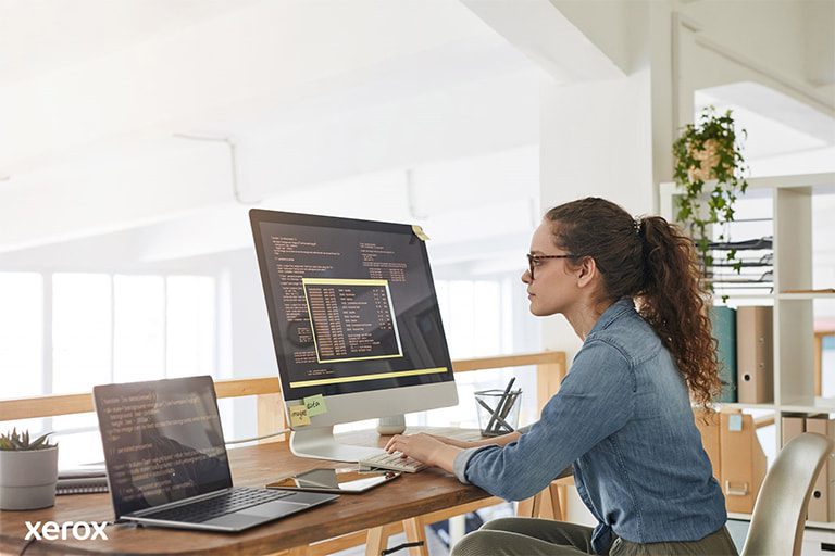 Una mujer sentada en su escritorio, con una computadora y una laptop, demostrando productividad en un espacio de trabajo moderno. Una mujer sentada en su escritorio, con una computadora y una laptop, demostrando productividad en un espacio de trabajo moderno.
