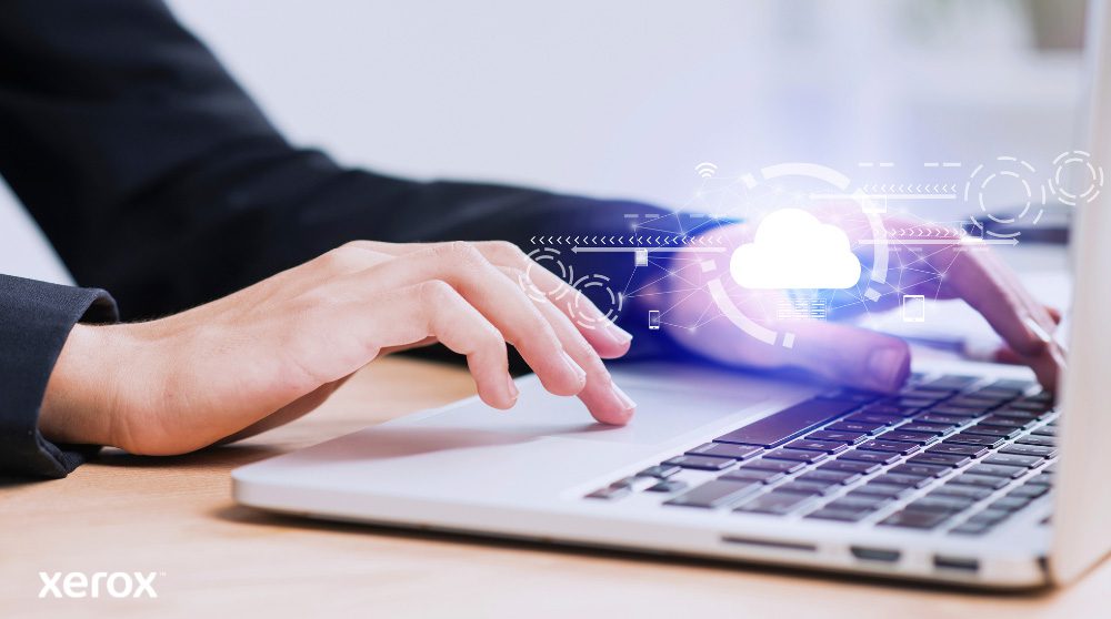 Se muestran las manos de una persona escribiendo en el teclado de una computadora portátil, con un ícono de nube brillante y conexiones de red superpuestas sobre la imagen, simbolizando la conectividad en la nube y los flujos de trabajo digitales.