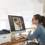 Una mujer sentada en un escritorio, concentrada en su trabajo, con una impresora Xerox® C320 a color