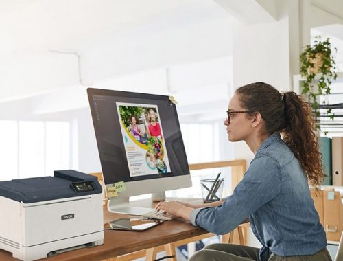 Una mujer sentada en un escritorio, concentrada en su trabajo, con una impresora Xerox® C320 a color