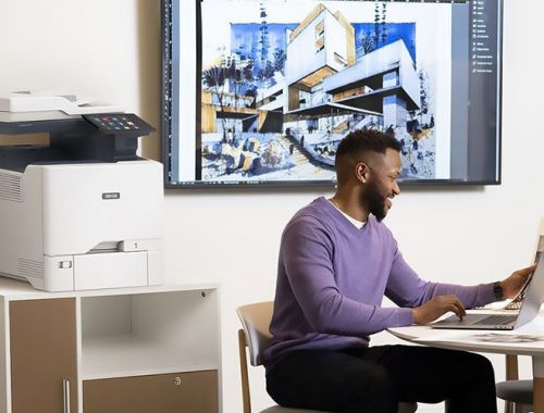 Hombre trabajando con un portátil delante de una impresora multifunción en color Xerox® VersaLink® C415