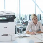 Impresora multifunción Xerox® VersaLink® C625 en una oficina Dos mujeres trabajando en una oficina junto a una impresora multifunción en color Xerox® VersaLink® C625