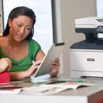 Impresora multifunción Xerox® VersaLink® B415 en la oficina Dos mujeres usando una tableta frente a una impresora multifuncional Xerox® VersaLink® B415