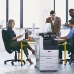 Equipo de trabajo en una oficina con papeles impresos y la impresora multifunción en color Xerox® Serie VersaLink® C7100