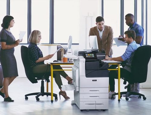 Equipo de trabajo en una oficina con papeles impresos y la impresora multifunción en color Xerox® Serie VersaLink® C7100
